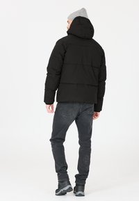 Svart vadderad jacka med huva, med quiltade sektioner och elastiska ärmslut, kombinerad med mörkgrå jeans och svarta vandringskängor.