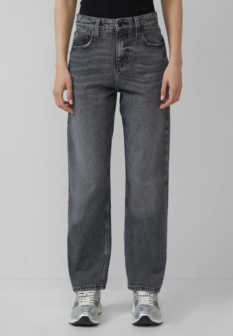 Jeans taille haute, coupe large en denim noir délavé. Caractéristiques incluent un design à cinq poches et des détails de couture subtils, associés à des baskets argentées.