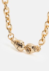 Colar de corrente dourada com um fecho decorativo em forma de duas mãos entrelaçadas, com detalhes gravados para adicionar textura.