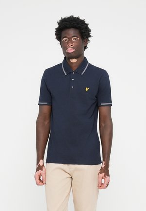 Polo shirt navy avec col et poignets gris, présentant un logo jaune sur la poitrine. Tissu lisse, manches courtes et design à boutons.