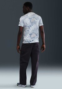 Camiseta de manga corta, de color claro, con un patrón abstracto azul en espiral, combinada con pantalones oscuros y holgados.