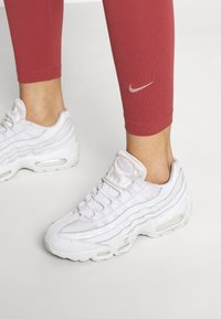 Vita Nike Air Max 95-sneakers med ett texturerat mesh- och läderöverdrag, med synliga luftkuddar och en smal rosa logotyp på röda leggings.