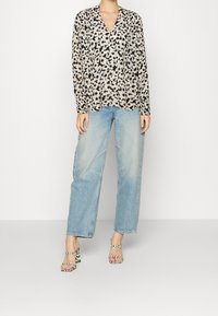 Blusa leggera a maniche lunghe beige con stampa leopardo nera, abbinata a jeans a gamba larga azzurri. Sandali con tacco bianco e nero a fantasia.