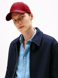 Rode baseballpet met logo, gedragen met een marineblauwe wollen jas en een lichtblauwe spijkerblouse, met een ritssluiting aan de voorkant en knoopdetails.