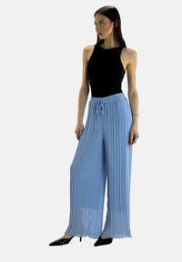 Jasnoniebieskie plisowane spodnie z szerokimi nogawkami, z elastycznym pasem i sznurkiem do wiązania. Połączone z czarnym bezrękawnikiem i czarnymi szpilkami.