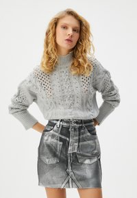 Jasnoszary sweter z dzianiny, ze wzorem w warkocze i detalami ażurowymi, zestawiony z czarną spódnicą jeansową o wysokim stanie, z wyblakłym wzorem i strzępionym dołem.