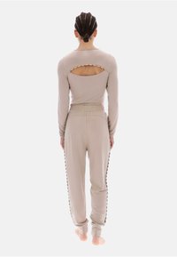 Zestaw beżowej odzieży wypoczynkowej w jasnym odcieniu, składający się z długiego topu z ozdobnym wycięciem i dopasowanych spodni dresowych z bocznymi guzikami.
