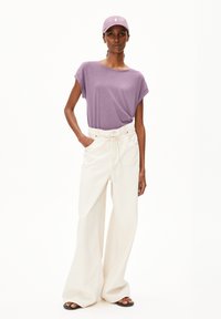 Purple short-sleeve shirt, loose-fitting white wide-leg pants, pink cap with logo, and black sandals. Flat fabric textures, casual design.