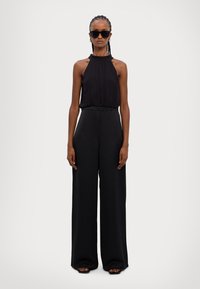 Black halter top with gathered neckline, paired with wide-leg black trousers. Smooth fabric, minimalistic design, and no visible patterns.