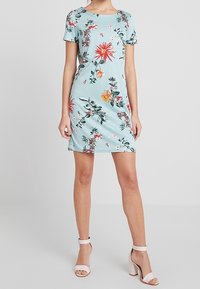 Květinové šaty z světle modré látky, krátké rukávy a přiléhavý střih. Disponují červeným a žlutým květinovým vzorem a kulatým výstřihem.