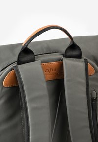 Grauer Rucksack aus Stoff mit braunen Lederakzenten, ausgestattet mit gepolsterten Trägern, einem oberen Griff und einer Reißverschlusstasche zur Aufbewahrung.