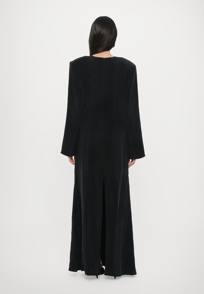 Robe noire longue avec une texture lisse, encolure en funnel, manches longues et fente au dos. Dispose d'une fermeture éclair discrète au dos.