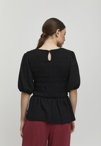 Sort peplum-top med struktureret stof, der har en nøglehulåbning bagpå og puffede ærmer. Sættes sammen med løstsiddende bordeaux bukser.