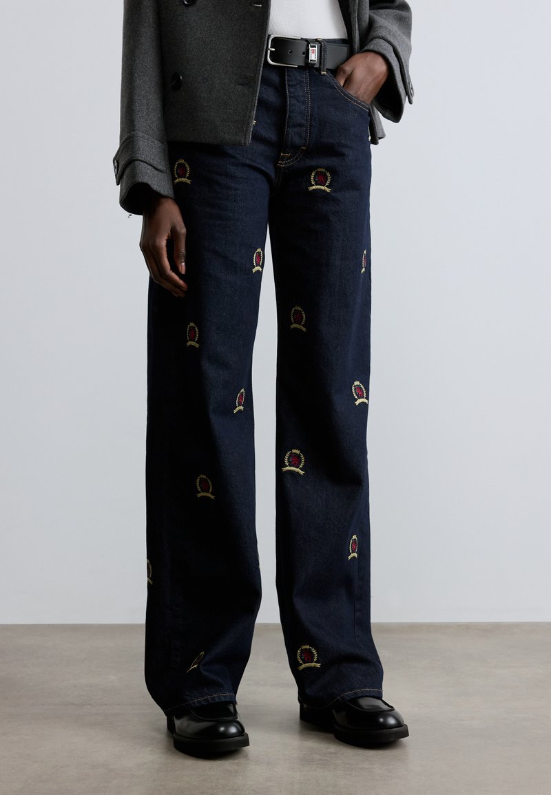 Tume sinised laiade säärtega teksapüksid, millel on tikandid kroonidest punases ja kuldsetes toonides. Valmistatud siledapinnalisest teksariidest. Sobitatud mustade jalanõudega.