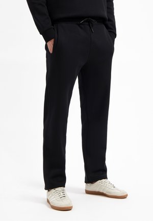 Zwarte sweatpants van zacht materiaal, met zijzakken en een elastische tailleband met trekkoord. Gepaard met lichte sneakers.