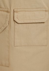 Khaki stof met een gladde textuur heeft twee grote, rechthoekige zakken. De stiknaad is zichtbaar in een contrasterende draadkleur.