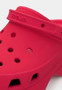 Calçado estilo Crocs cor-de-rosa feito de material flexível, com múltiplos orifícios de ventilação, sola com textura antiderrapante e logótipo em relevo na tira.
