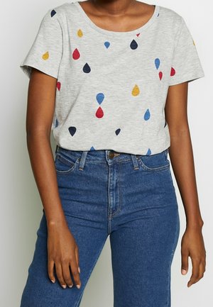 Szara koszulka z krótkim rękawem, ozdobiona kolorowymi wzorami kropli w kolorach czerwonym, niebieskim, żółtym i czarnym. Noszona z niebieskimi dżinsami z wysokim stanem.
