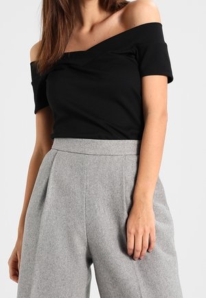 Sort off-shoulder top med korte ærmer, parret med højhvide grå uldbukser med folder og en glat stoftekstur.