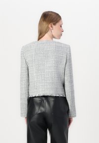 Siva tweed jakna s krojenjem iznad struka, s rubom koji se koristi, i dugim rukavima. Uparena s crnim kožnim hlačama, koje ističu teksturiranu završnu obradu.