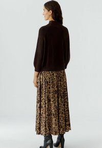 Bruine gebreide trui met geribbelde textuur, gecombineerd met een lange, geplisseerde rok in bruin en tan met een luipaardprint. Zwarte haklaarzen maken de look compleet.