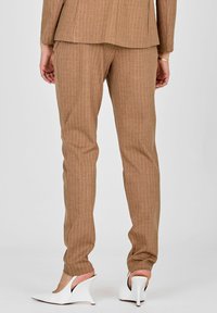 B Raočene hlače z rjavimi črtami iz teksturirane tkanine, zožen kroj, v kombinaciji z belimi čevlji s konicami.
