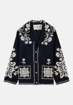 Veste marine avec broderies florales blanches, poches carrées et fermeture à boutons. Le matériau semble texturé et durable, avec un design de col classique.