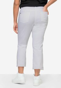 Pantaloni grigi tagliati con orlo grezzo, dotati di tasche posteriori; abbinati a sneaker bianche alte. Tessuto liscio con texture minima.