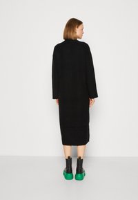 Abito maxi nero in maglia con maniche lunghe e scollo rotondo. Indossato con stivaletti neri alla caviglia con suole verdi.