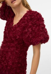 Bordowa sukienka z bufkami na rękawach, pokryta warstwami kwiatów z tkaniny. Dekolt w serek, miękka tekstura i misternie wykonane kwiatowe zdobienia.