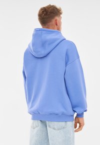 Felpa blu con cappuccio, dal fitting morbido, con polsini e orlo a costine. Tessuto liscio, branding minimal sull'apertura del cappuccio.