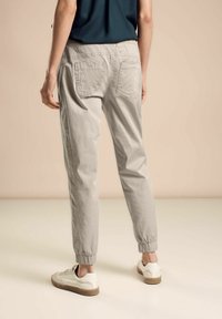 Ljusgrå joggbyxor i bomullsblandning med elastiska avslut, två bakfickor och en avslappnad passform, som bärs med vita sneakers.