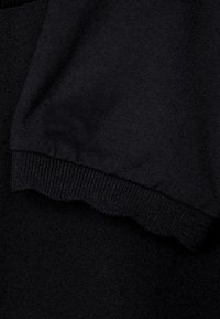 Svart textiltyg med en slät yta och ribbade kanter. Designen har ett vågigt avslut vid ärmen, vilket förbättrar det visuella detaljerna.