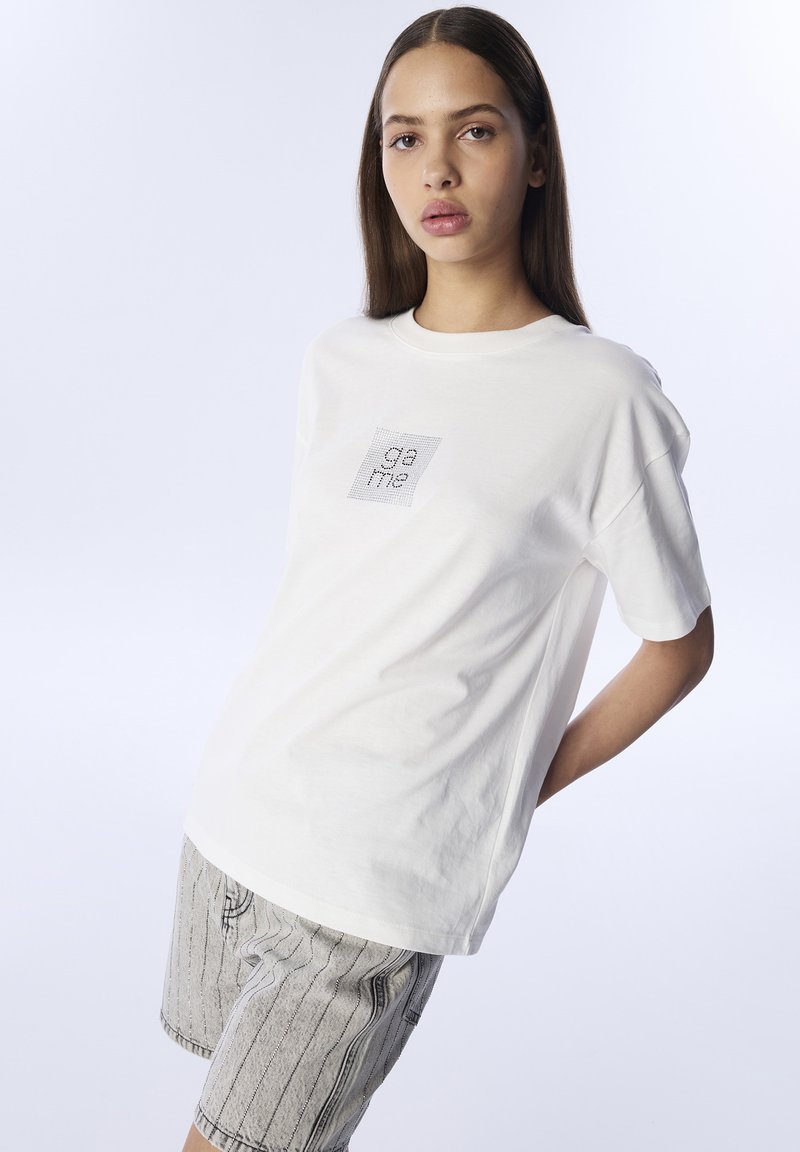 Camiseta de algodón blanca con cuello redondo y mangas cortas. Presenta un logo impreso con un diseño de rejilla en la parte frontal.