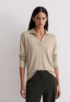 Maglietta a maniche lunghe beige chiaro con scollatura a V e colletto, realizzata in un tessuto morbido che scende leggermente, abbinata a pantaloni scuri a vita alta.