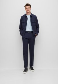 Μαρινί μπουφάν με δύο μπροστινές τσέπες, ανοιχτό μπλε πουκάμισο, ναυτικές παντελόνες και μαύρα αθλητικά παπούτσια. Το ύφασμα φαίνεται λείο με κομμένα ρούχα.