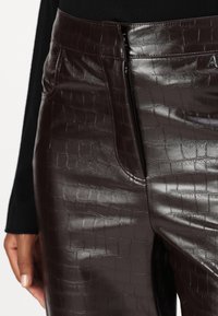 Braune Kunstlederhosen mit Krokodilprägung, ausgestattet mit einem Reißverschluss vorne und seitlichen Taschen. Glatte Oberfläche mit passformbetontem Design.