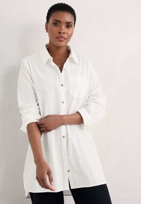 Biała koszula z długim rękawem, wykonana z lekkiego materiału, z kołnierzykiem i kieszonką z przodu. Złote akcenty w postaci guzików dopełniają projekt.