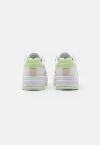 Sneakers bianchi con accenti crema e verde, texture liscia, suola chunky bianca e branding sottile sul tallone e sul lato.