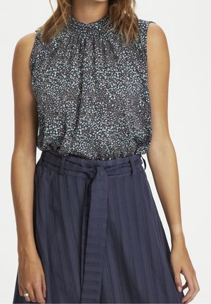 Ærmeløs mørk blomsterprintet højhalset top kombineret med højtaljede marineblå viddebenbukser med lodrette striber og et bundet stofbælte.