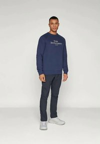 Σκούρο μπλε φούτερ με κείμενο "Peak Performance", μακριά μανίκια,  ribbed cuffs και στρίφωμα, σε συνδυασμό με σκούρα παντελόνια και ανοιχτόχρωμα αθλητικά παπούτσια.