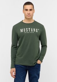 Hosszú ujjú, sötétzöld pamut ing, fehér "MUSTANG" logóval és szöveggel, kerek nyakkivágással, laza szabással és sima felülettel.