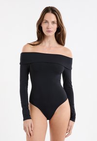 Body noir à manches longues avec un décolleté épaules nues. Tissu lisse, coupe ajustée, ouverture haute à la jambe, détails minimalistes.