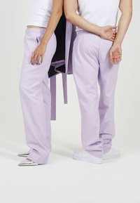 Lavender hlače v sproščenem kroju, narejene iz lahkotnega materiala. Imajo elastičen pas in so kombinirane s srebrnimi in belimi čevlji.