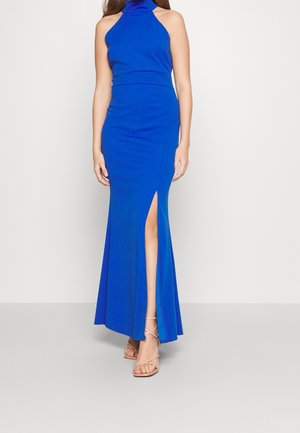 Blauwe halternek maxi-jurk van rekbare stof, met een nauwsluitend lijfje, uitlopende rok en zijspal. Gecombineerd met nude hakken met bandjes.