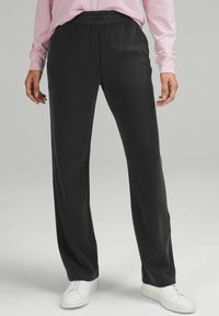 Svarta, vida byxor i ett mjukt och lätt tyg med resårmidja och dragsko. Stylen kompletteras med vita sneakers.