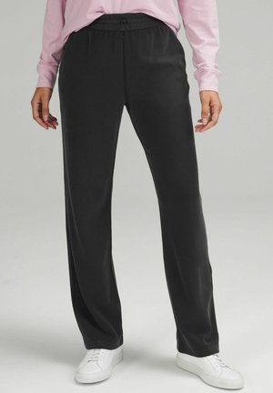 Svarta, vida byxor i ett mjukt och lätt tyg med resårmidja och dragsko. Stylen kompletteras med vita sneakers.