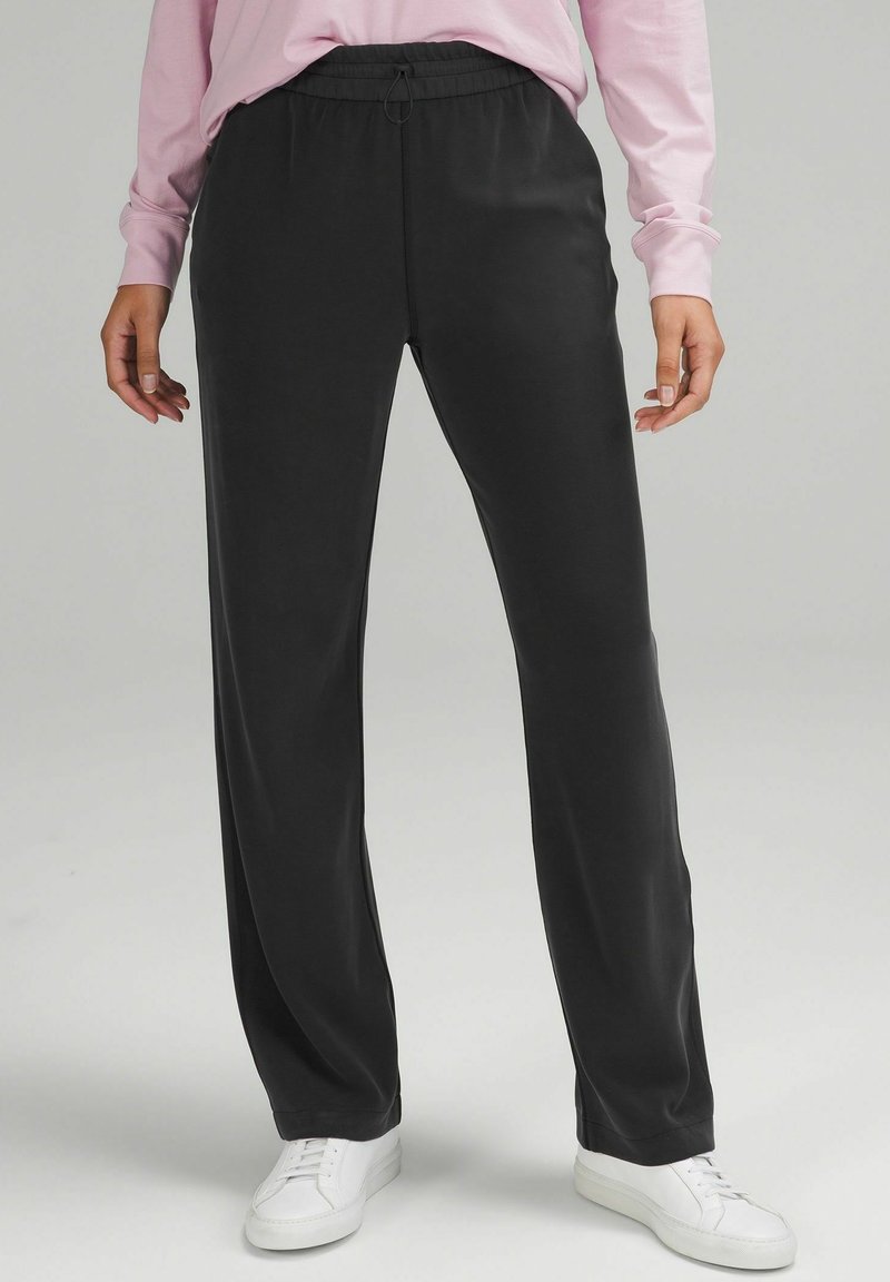 Svarta, vida byxor i ett mjukt och lätt tyg med resårmidja och dragsko. Stylen kompletteras med vita sneakers.