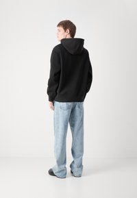 Hanorac negru cu glugă, cu o croială lejeră, asortat cu blugi de tip wide-leg de culoare albastru deschis. Materialul pare moale; design simplu, fără modele vizibile.