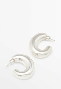 Boucles d'oreilles en métal argenté avec un design lisse et courbé évoquant une forme de croissant, avec une finition polie et un attache arrière.